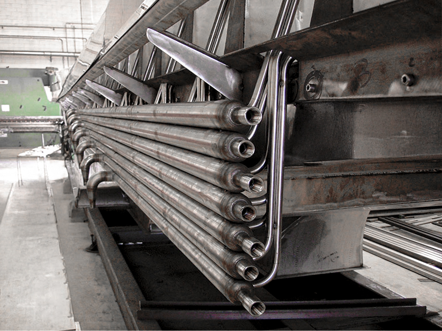 Vista ravvicinata di tubi metallici piegati in uno schema preciso e ripetuto e fissati a una macchina industriale all'interno di una fabbrica.